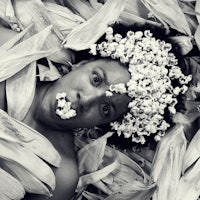 a black and white photo of a woman covered in corn leaves