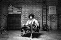 a woman sitting on a chair in front of a brick wall