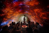 a group of people sitting in a tunnel with a starry sky